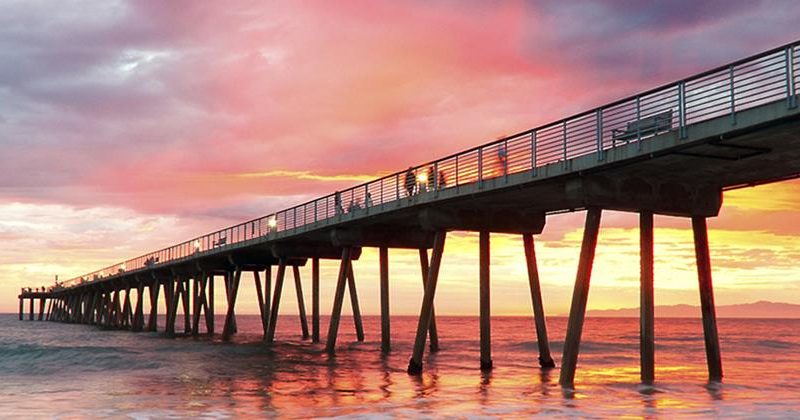 Sun setting behind a boardwalk reaching out into the ocean representing improved performance and achievement