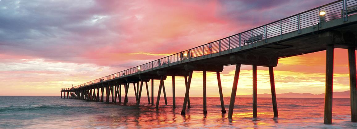 Sun setting behind a boardwalk reaching out into the ocean representing improved performance and achievement